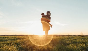 a father holds a child in his arms at sunset