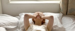 A woman in a white dress lies on her bed, reflecting on her thoughts amid the anxiety of the current coronavirus situation.