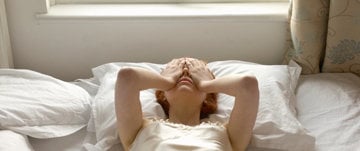 A woman in a white dress lies on her bed, reflecting on her thoughts amid the anxiety of the current coronavirus situation.