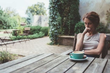 A woman sits on a bench, sipping coffee, reflecting on managing anger and guilt as a caregiver.