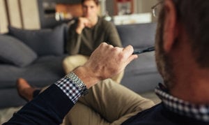 A man on a couch, engaged with his pen, contemplating his views on therapy misconceptions.