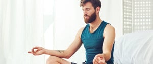 A man sits in a yoga pose on a bed, meditating peacefully, representing strength and mindfulness in difficult moments.