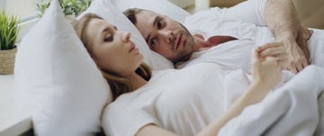  A man and woman lying in bed together, sharing a moment of comfort and support amidst discussions of anxiety.