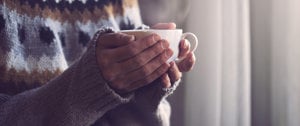 Individual cradling a coffee cup, contemplating the effects of weather changes on migraine symptoms.