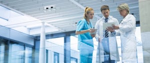 A group of doctors and nurses stands confidently in front of a glass wall, symbolizing collaboration in the medical field.