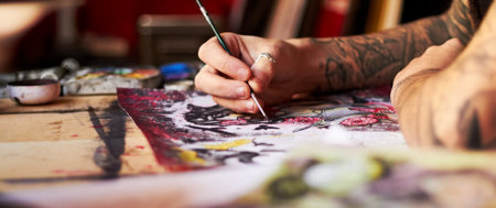 Close-up of a tattooed artist's hands painting on canvas.