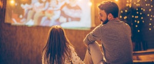 A man and a little girl are seated on the floor, enjoying a movie together in a cozy setting.