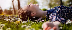 A woman reclines in a field of daisies, finding peace amidst nature while managing migraine anxiety.