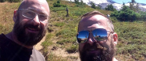 Two bearded men in sunglasses take a selfie, celebrating life after overcoming a heart attack.