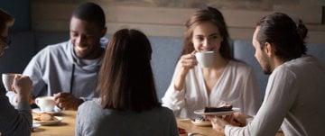 A group of individuals gathered around a table, enjoying coffee and engaging in conversation, reflecting on mental health benefits.