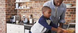 A man and a young boy collaborate in the kitchen, preparing food together, showcasing a moment of shared learning and bonding.