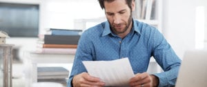 A man examines a document at his desk, reflecting on the hidden costs of caregiving.