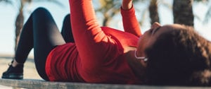 A woman lies on a bench with her arms raised, reflecting on her experience during her first asthma attack.