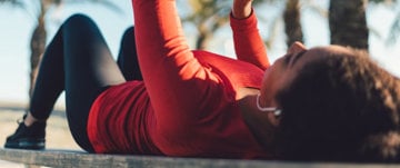 A woman lies on a bench with her arms raised, reflecting on her experience during her first asthma attack.