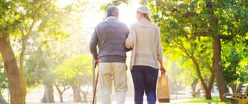 An older couple strolls hand in hand through a serene park, embodying the joys of companionship and caregiving.