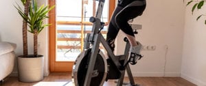 A woman exercises on a stationary bike in a room, adapting to the 'New Normal' while managing multiple sclerosis.