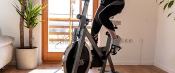 A woman exercises on a stationary bike in a room, adapting to the 'New Normal' while managing multiple sclerosis.