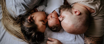 A man and woman lie on a bed with their baby, illustrating the challenges of parenting amid mental health struggles.