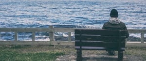 A person seated on a bench gazes thoughtfully at the vast ocean before them, surrounded by serene natural beauty.