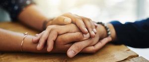 Two individuals holding hands on a wooden table, symbolizing support and connection during migraine challenges.