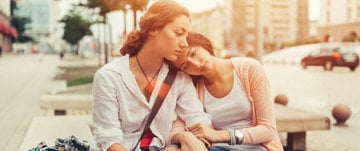 Two women sit on a bench, sharing a moment, with a quote about the joys of being in a relationship displayed above them.