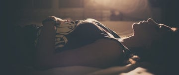 A woman resting in bed with her eyes closed, coping with the discomfort of a migraine.