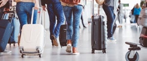 Passengers navigate through an airport terminal, each carrying luggage, reflecting the dynamic environment of travel.