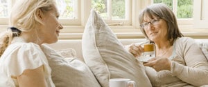 Two women sit together on a couch, sipping coffee and reflecting on the lessons of friendship learned through an MS diagnosis.