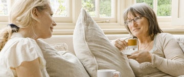 Two women sit together on a couch, sipping coffee and reflecting on the lessons of friendship learned through an MS diagnosis.