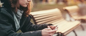 A woman sits on a bench, absorbed in her phone, reflecting on managing social media amid depression and anxiety.