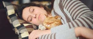 A woman lies asleep with a cat on her chest, symbolizing tranquility and the importance of rest in managing MS fatigue.