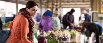 A woman shopping for fresh produce at a farmers market, embracing nutritious choices that support her asthma improvement journey.