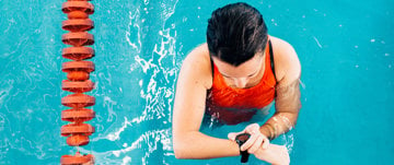 A woman wearing a watch enjoys swimming in a pool, symbolizing active living during and after cancer treatment.