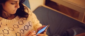 A woman on a bed gazes at her phone, contemplating methods for managing intrusive thoughts effectively.