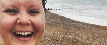 A woman smiles confidently on the beach, embodying strength and joy in her journey of reclaiming her body after cancer.