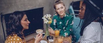 three friends are sitting at the table and talking drinking coffee and juice