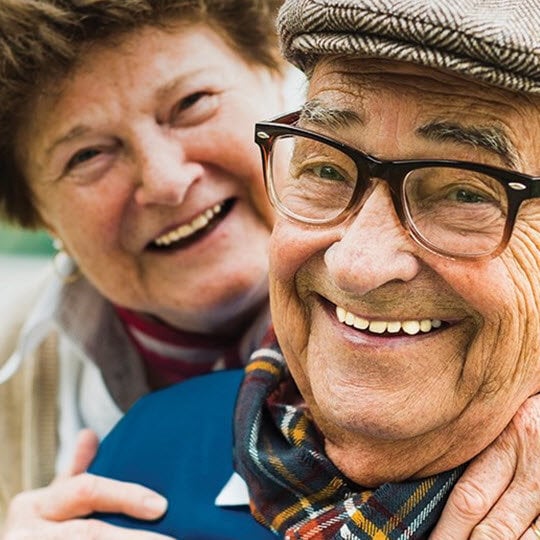 An older couple smiles warmly while embracing each other, showcasing their affection and joy in a heartfelt moment.