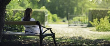 A woman relaxes on a park bench, symbolizing the challenges of living with MS during the summer season.