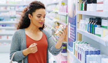 A woman examines a shelf filled with various medicine bottles in a well-lit pharmacy setting.