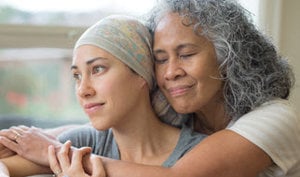 A woman in a headscarf stands beside an older woman, symbolizing support and care in the context of cancer caregiving.