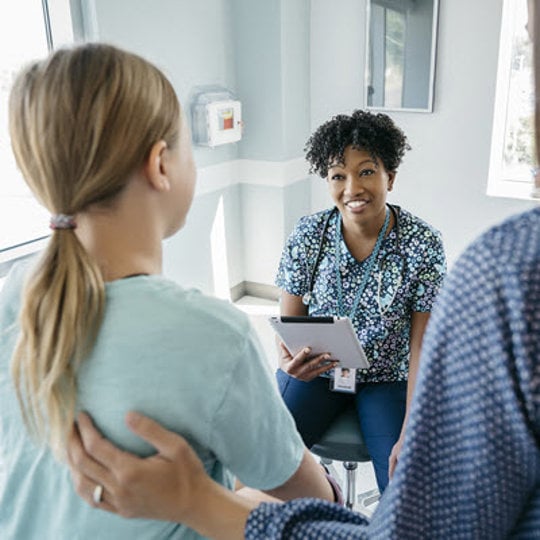 A nurse engages in conversation with a patient in a hospital room, providing care and support during their recovery.