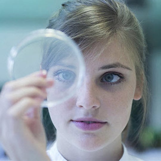 A woman in a lab coat holds a magnifying glass, illustrating her focus on the research and understanding of biosimilars.