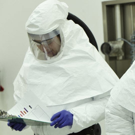 Two individuals wearing protective suits and white coveralls, ensuring safety in a controlled environment.